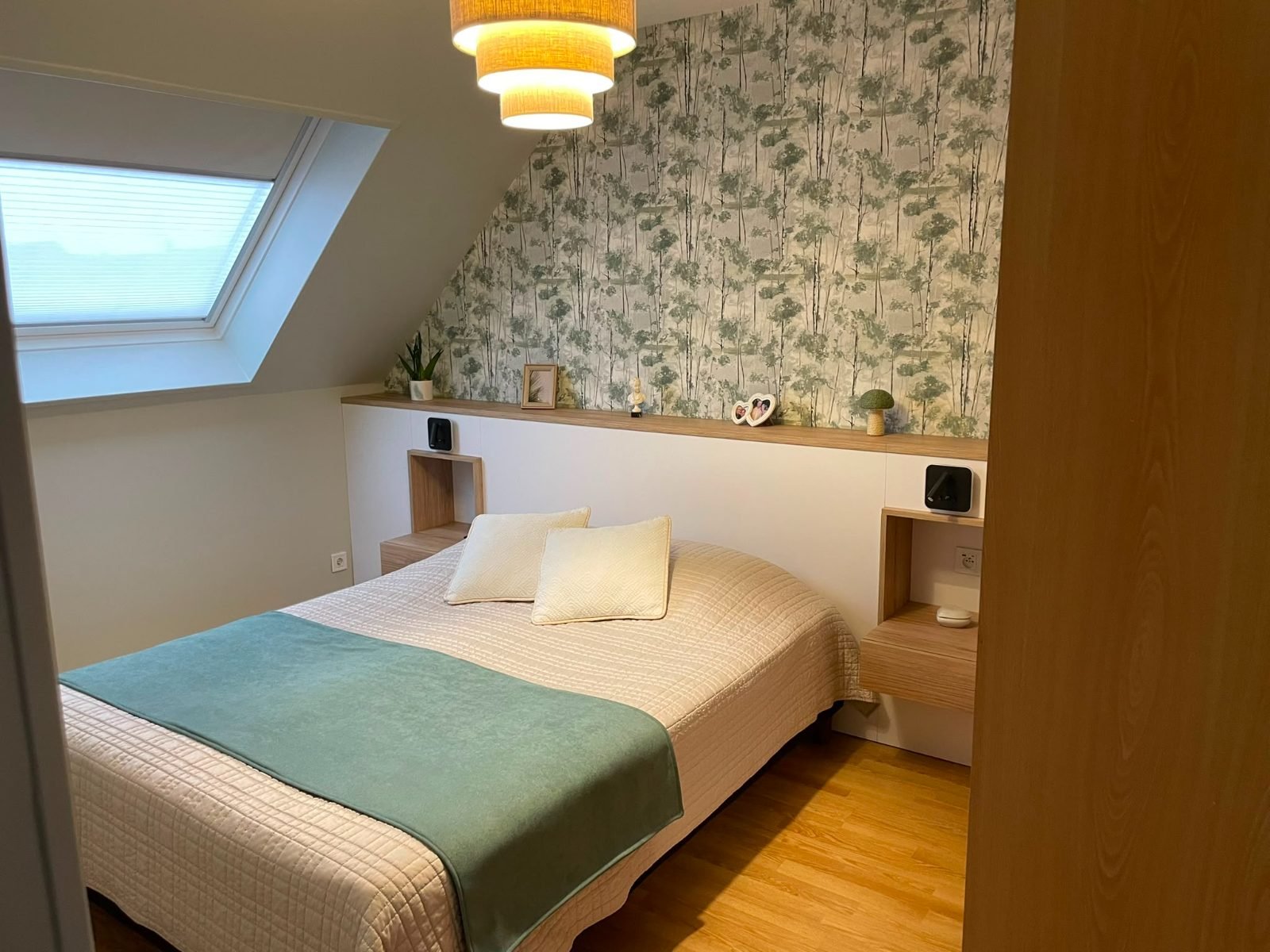 Chambre sous pente — papier peint forêt, tête de lit blanche et bois, fenêtre de toit